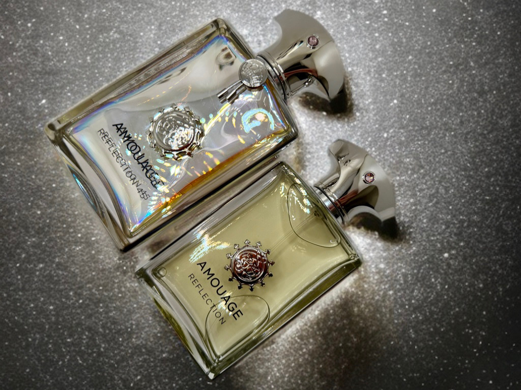 Amouage Reflection Man und Amouage Reflection 45 stehen nebeneinander auf einem hellen Hintergrund. Beide Flakons zeigen den Kontrast zwischen der frischen Eleganz von Reflection Man und der warmen Tiefe von Reflection 45.
