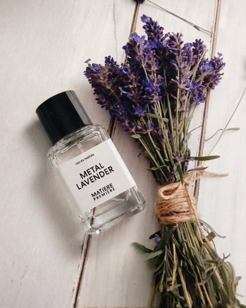 Metal Lavender Matière Première Parfum Flakon neben Lavendelstrauß auf hellem Holzuntergrund